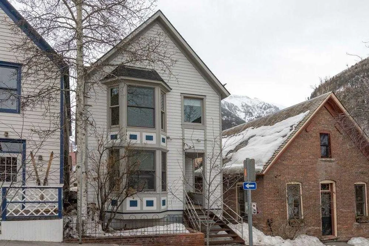 A picturesque Victorian-style building set against snow-covered ground and surrounding mountains. The scene evokes a classic winter getaway with inviting architecture and a sense of community warmth.