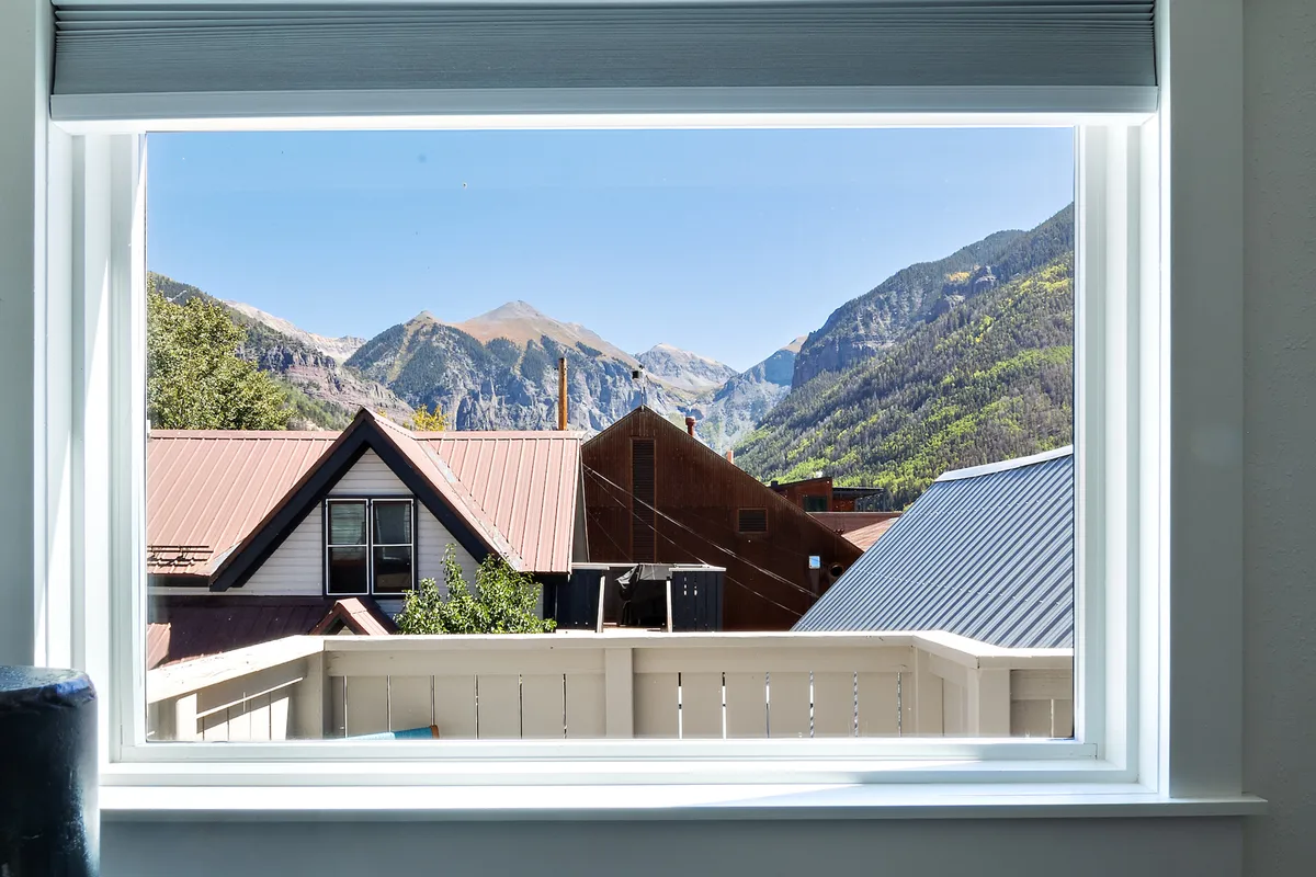 A serene view from a balcony overlooking a mountain range, rooftops, and trees, capturing the peaceful moments between festival activities. The perspective suggests a private perch where guests can relax and recharge while staying connected to the buzz below.